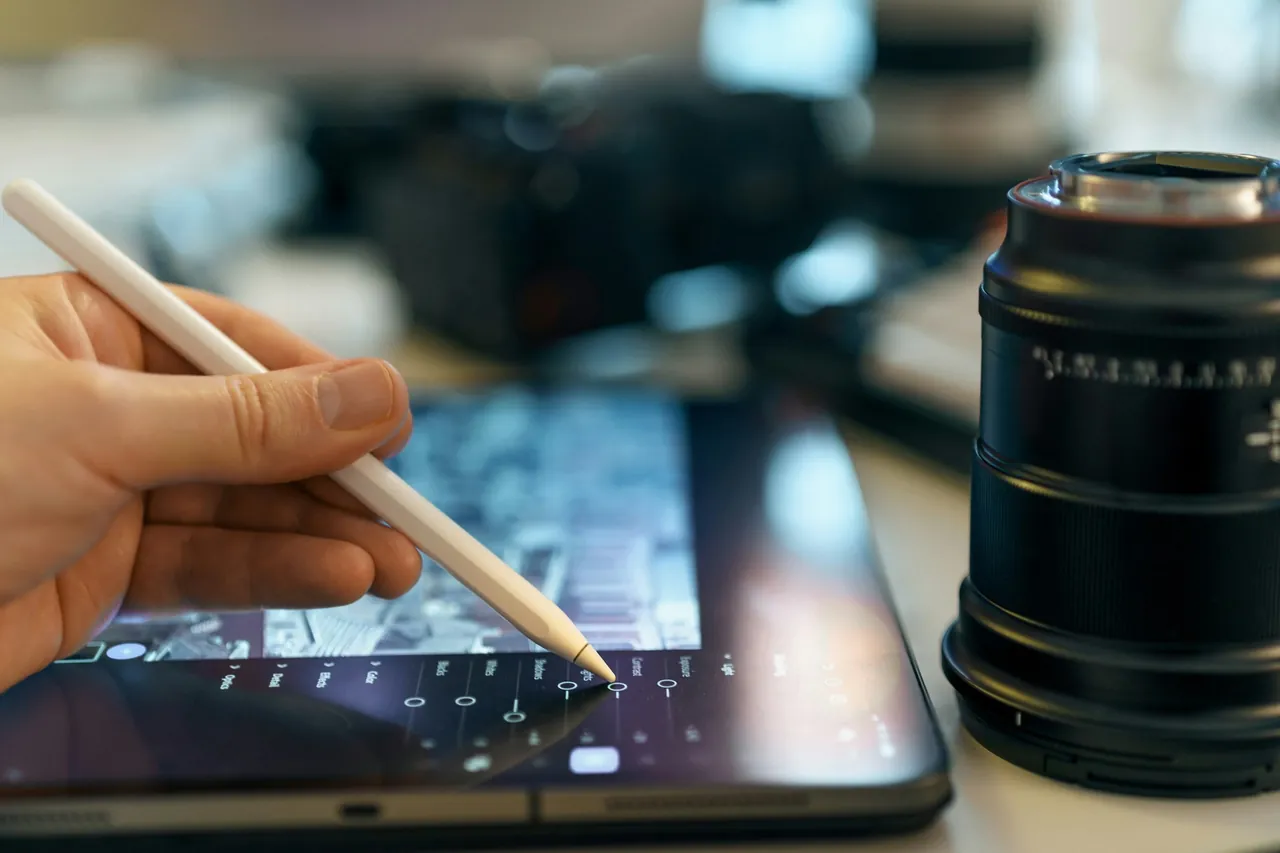 A hand editing on a tablet beside a camera lens